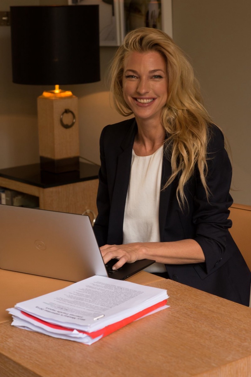 Nicole Junkermann in a navy blazer, smiling warmly at a laptop on a lamp-lit desk